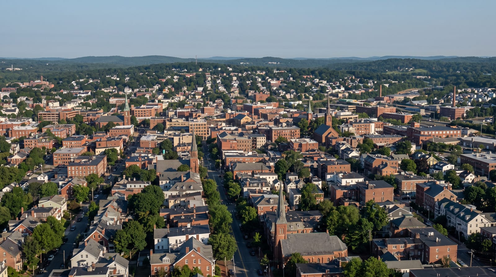 A wide daytime view across a New England city and the hills beyond