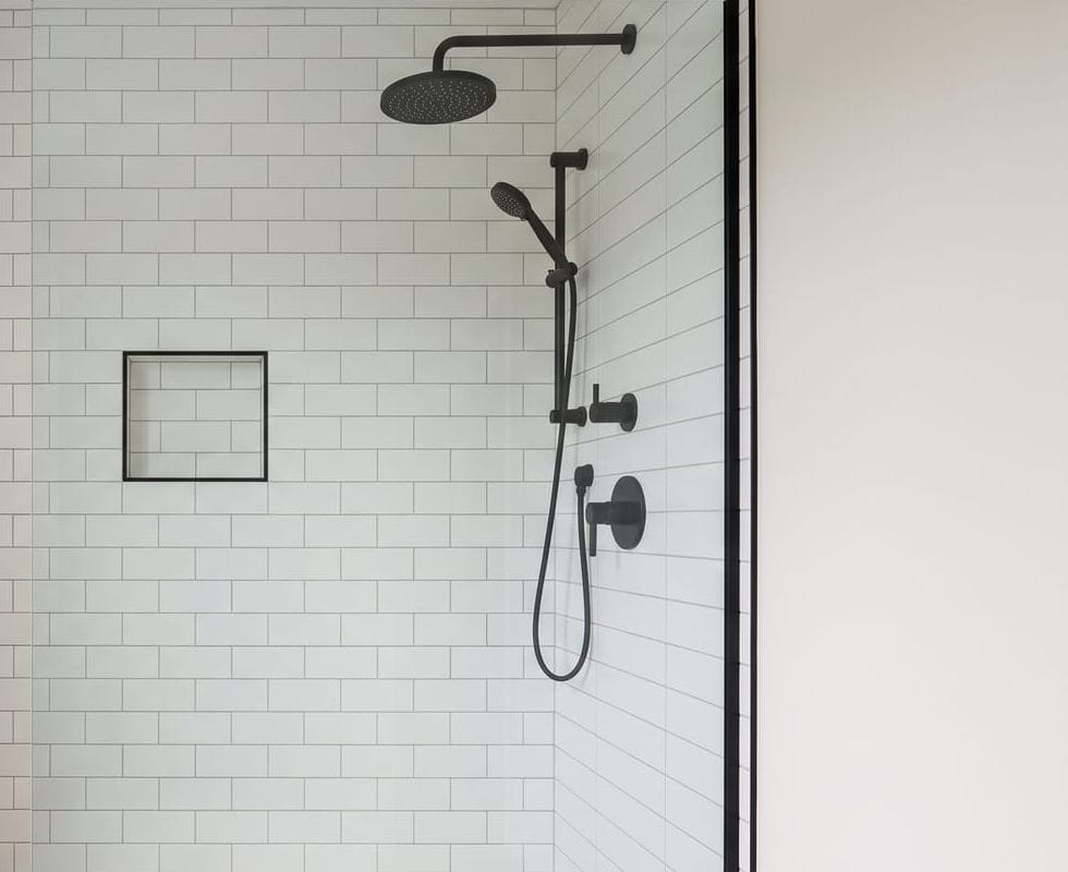 A recessed tiled niche and matte black shower fittings inside a walk-in shower